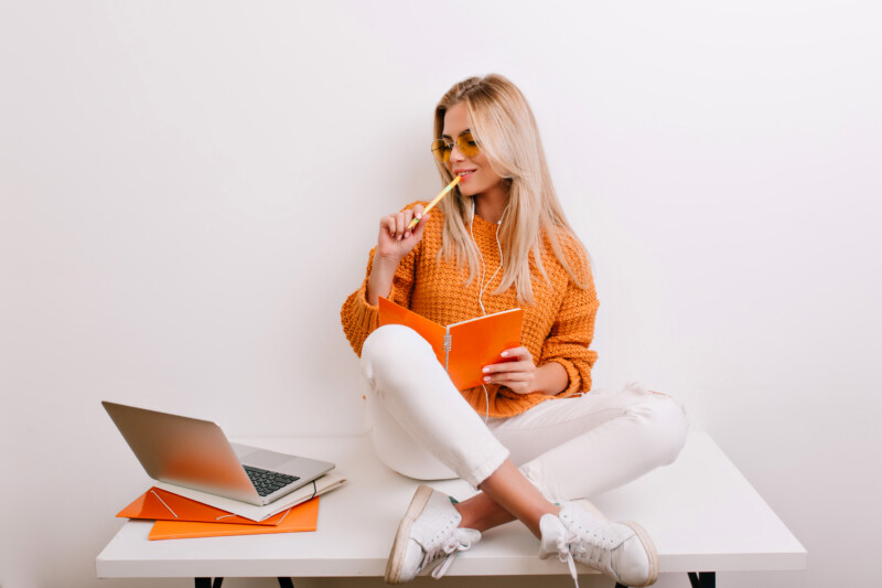 glad-fair-haired-woman-trendy-outfit-doing-her-job-office-holding-notebook-pen